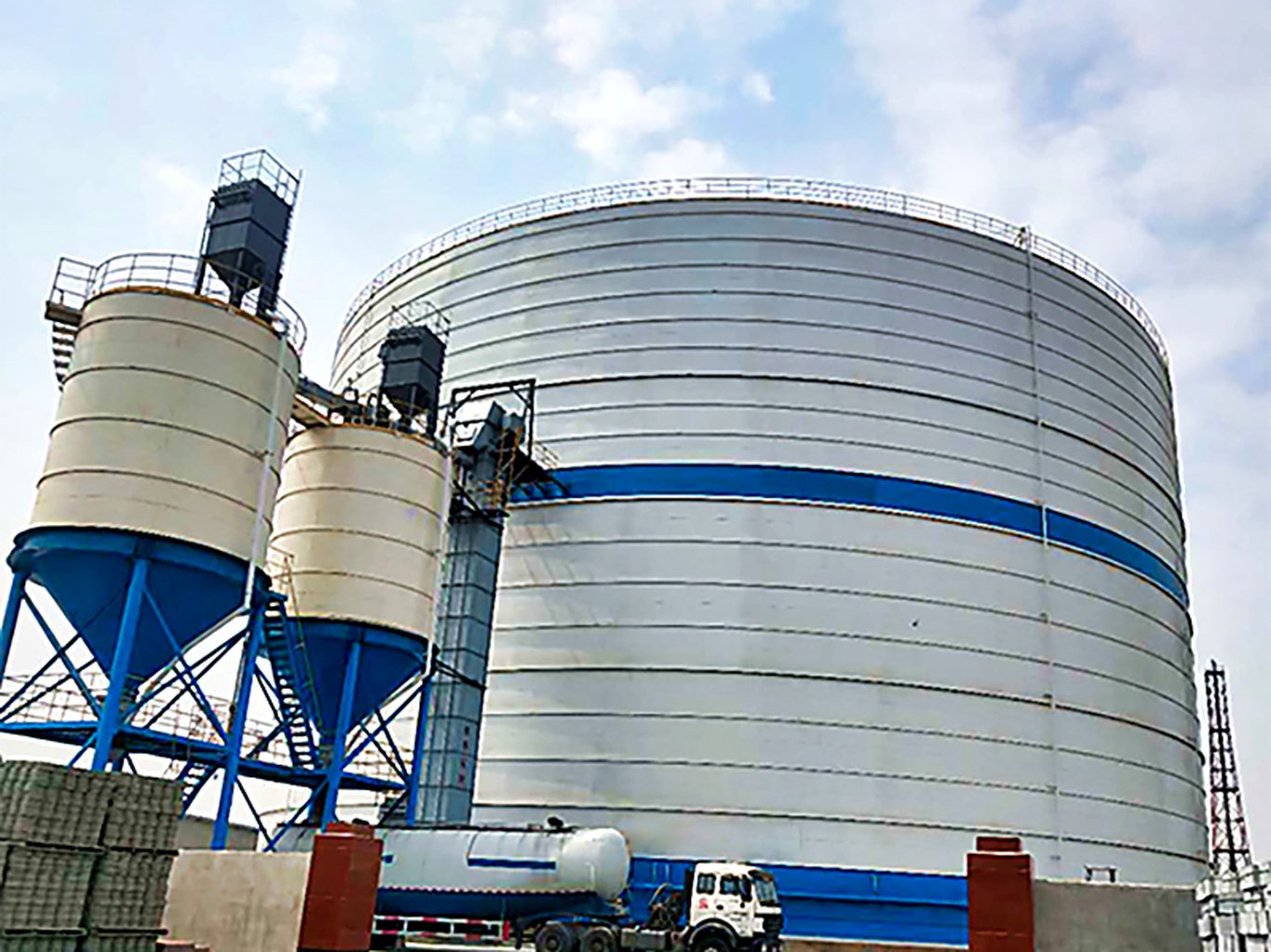Large flat-bottom welded steel silo with bulk truck unloading at a fly ash storage facility