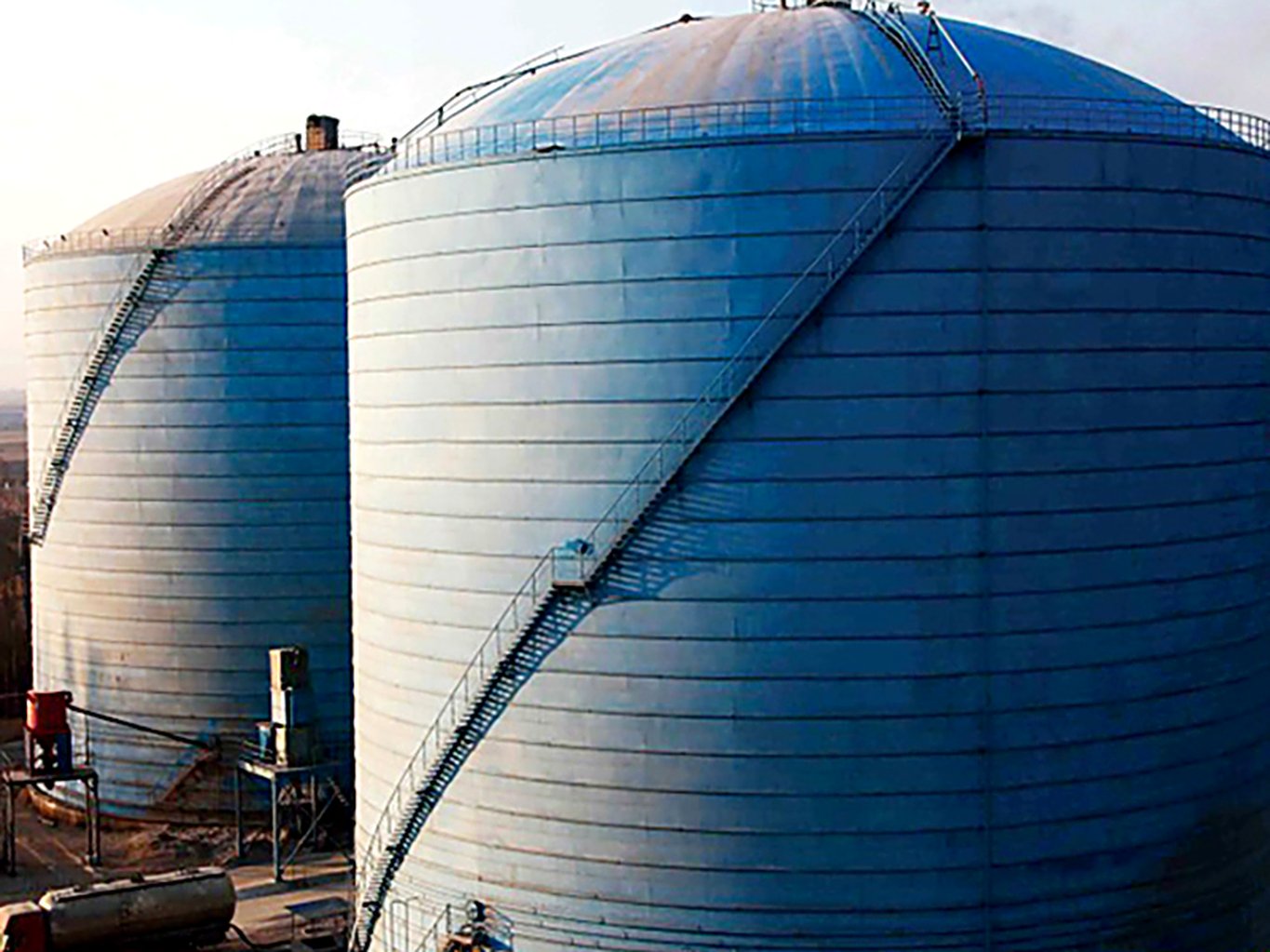 Large flat-bottom welded steel silos receiving bulk cement from road tankers at a distribution terminal