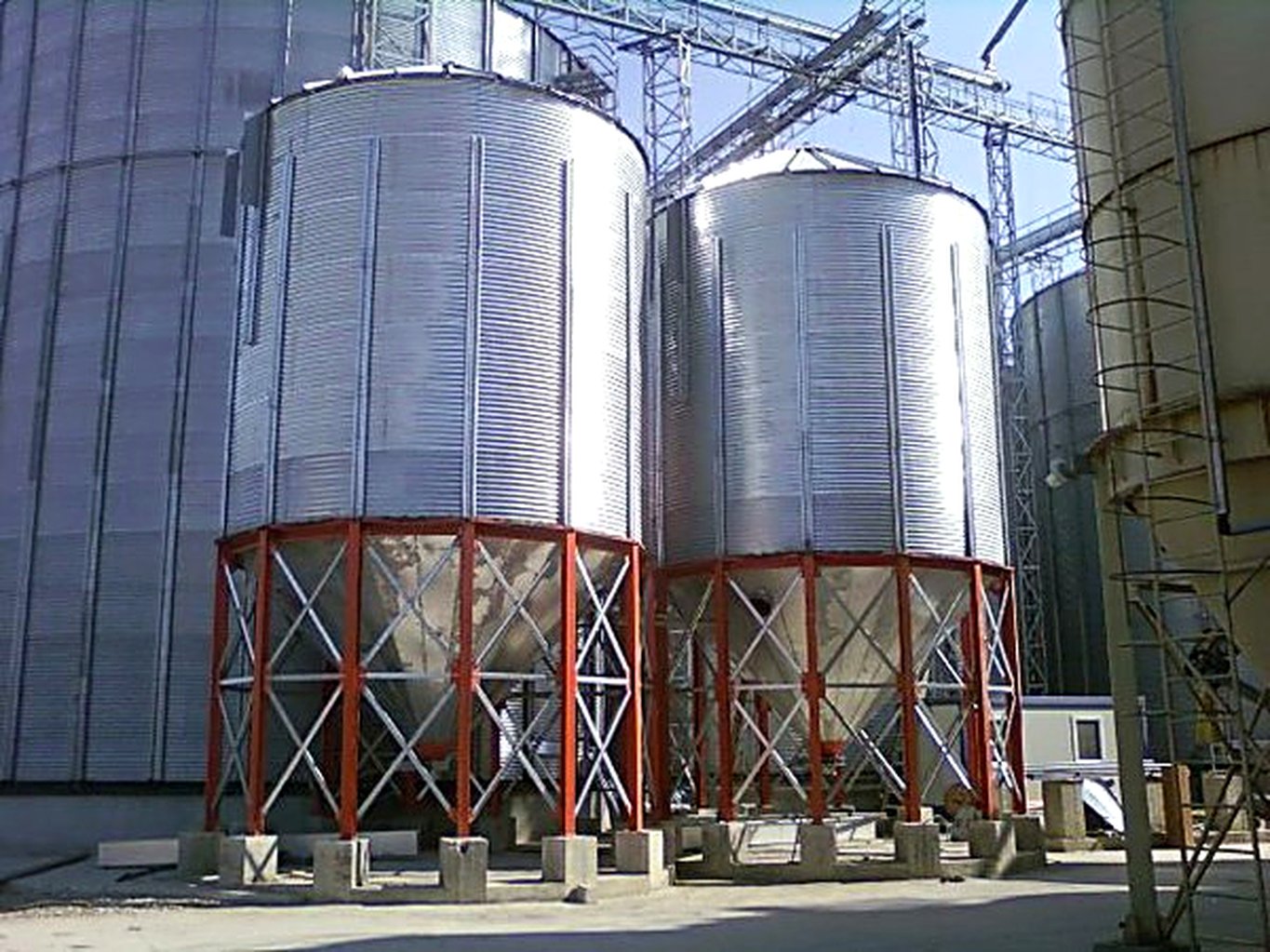 Hopper-bottom steel farm bins on support legs serving a poultry feed operation
